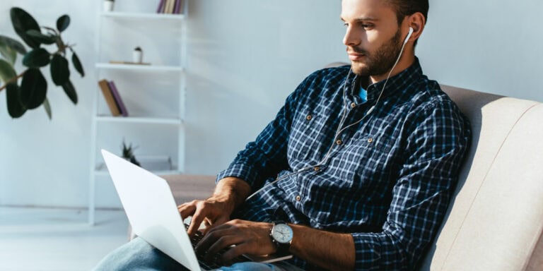 A man sitting on a couch using a laptop with headphones.