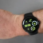 A smartwatch with a black band displays the time as 10:36 and various health metrics, worn on a person's wrist against a gray background.