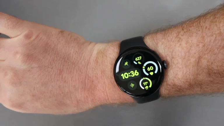 Eine Smartwatch mit schwarzem Armband zeigt die Uhrzeit 10:36 und verschiedene Gesundheitsmetriken an, getragen am Handgelenk einer Person vor einem grauen Hintergrund.