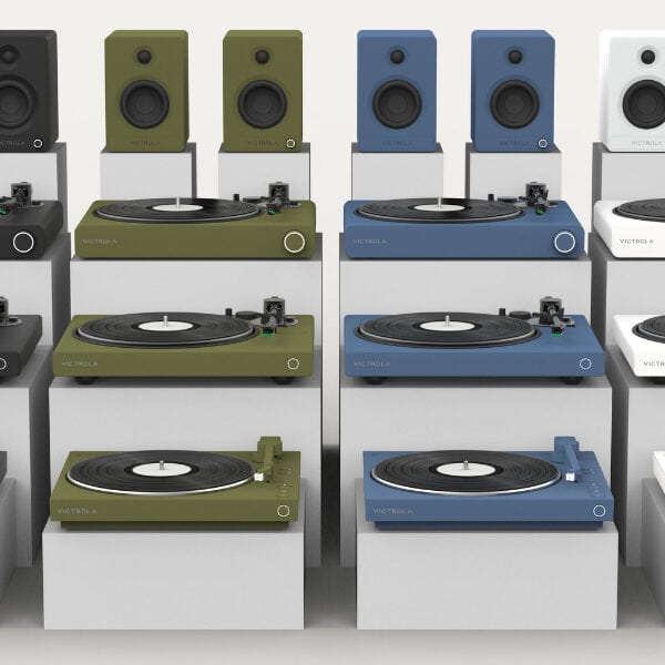 Display of various turntables and speakers in multiple colors including black, green, blue, and white, arranged on a white background.