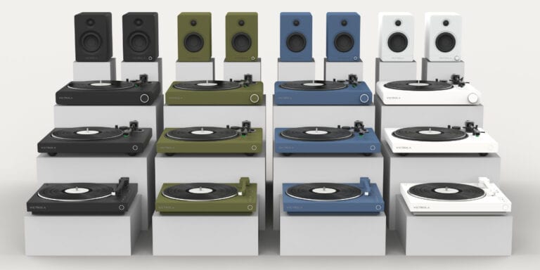 Display of various turntables and speakers in multiple colors including black, green, blue, and white, arranged on a white background.