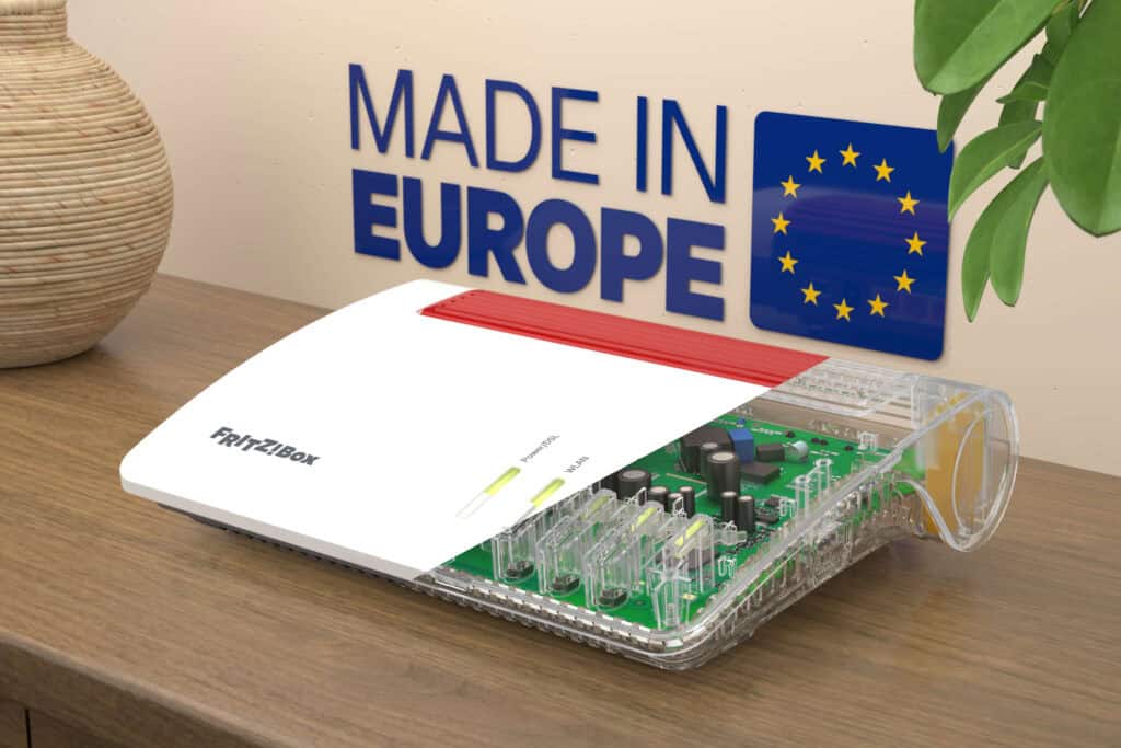 A FRITZ!Box router with a partially transparent cover showing internal components sits on a desk; "Made in Europe" and EU flag are displayed on the wall behind.