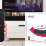 A hand holds a mobile displaying the Aura EZ logo; next to it is a Humax Aura EZ Ultra High Definition Recorder box on a white surface.