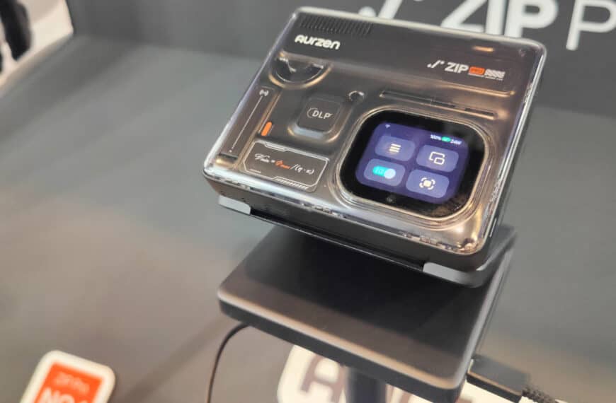 A compact digital camera labelled “Aurzen J’ZIP Pro” is displayed on a stand, showing a small touchscreen interface with various icons.