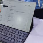 A person uses a tablet with a keyboard attached, displaying a digital note-taking app with handwritten notes in Chinese. Another person sits nearby, both wearing business attire.