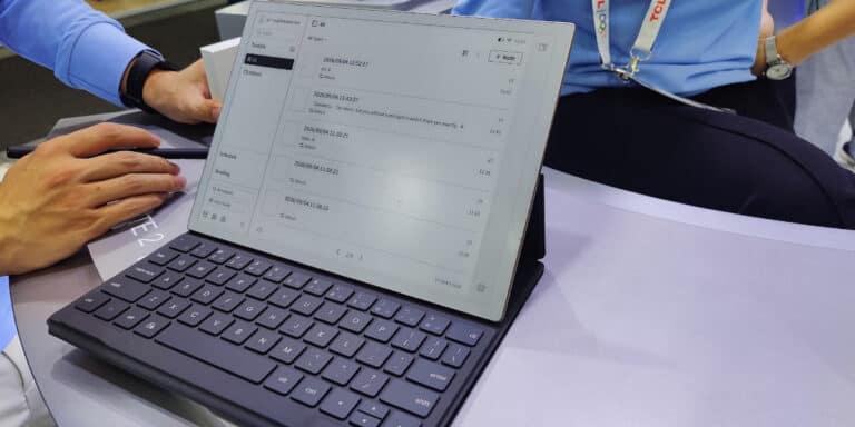 A person uses a tablet with a keyboard attached, displaying a digital note-taking app with handwritten notes in Chinese. Another person sits nearby, both wearing business attire.