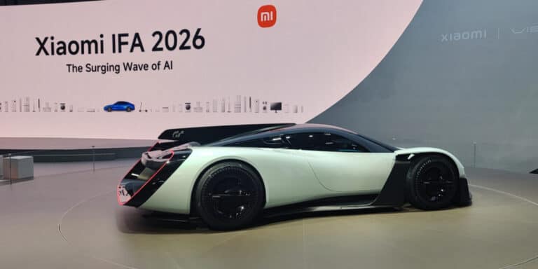 A futuristic white and black sports car is displayed at an indoor event with a large sign reading “Xiaomi IFA 2026 The Surging Wave of AI” in the background.