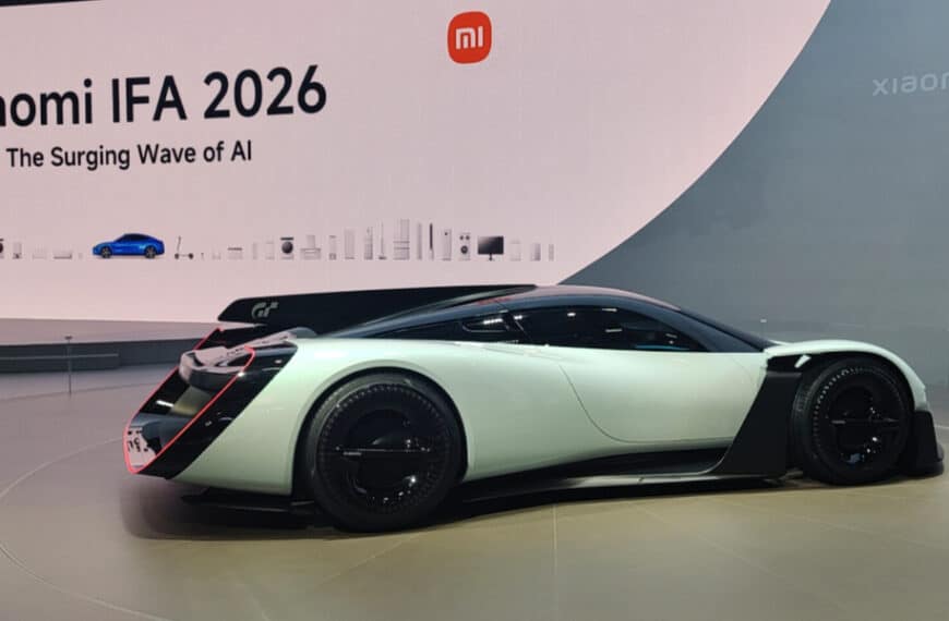 A futuristic white and black sports car is displayed at an indoor event with a large sign reading “Xiaomi IFA 2026 The Surging Wave of AI” in the background.