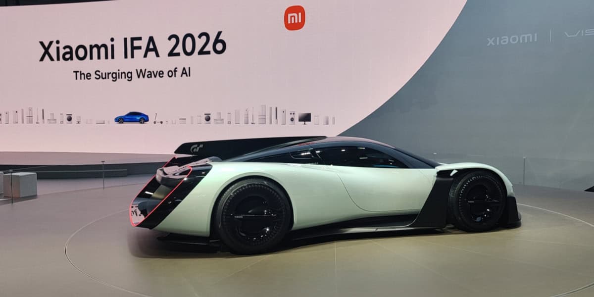 A futuristic white and black sports car is displayed at an indoor event with a large sign reading “Xiaomi IFA 2026 The Surging Wave of AI” in the background.